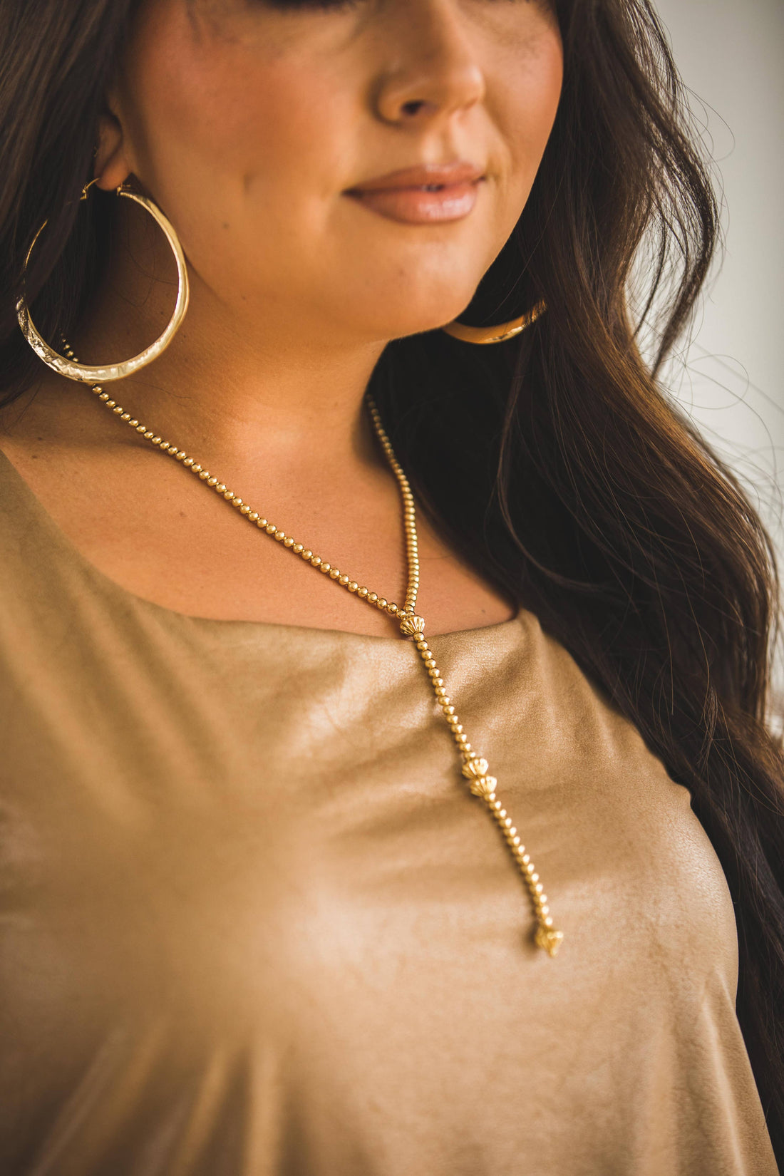 Woman wearing a gold necklace and hoop earrings with a neutral background