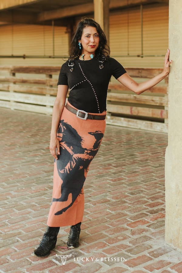 Woman in black top and patterned skirt standing on a brick pavement.
