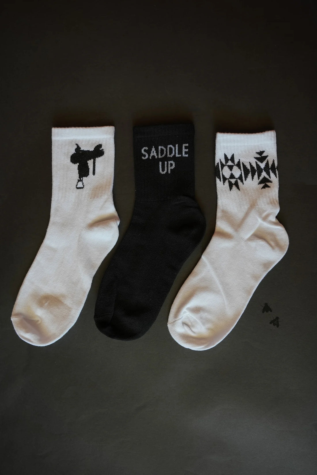 Western Vibe Socks Set featuring three unique designs: a saddle silhouette, &quot;Saddle Up&quot; text, and a geometric Western pattern. One size fits most.