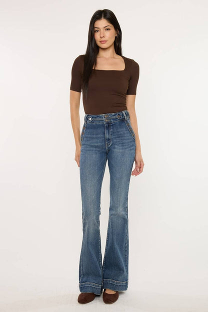 Woman wearing blue flared jeans and a brown top on a white background