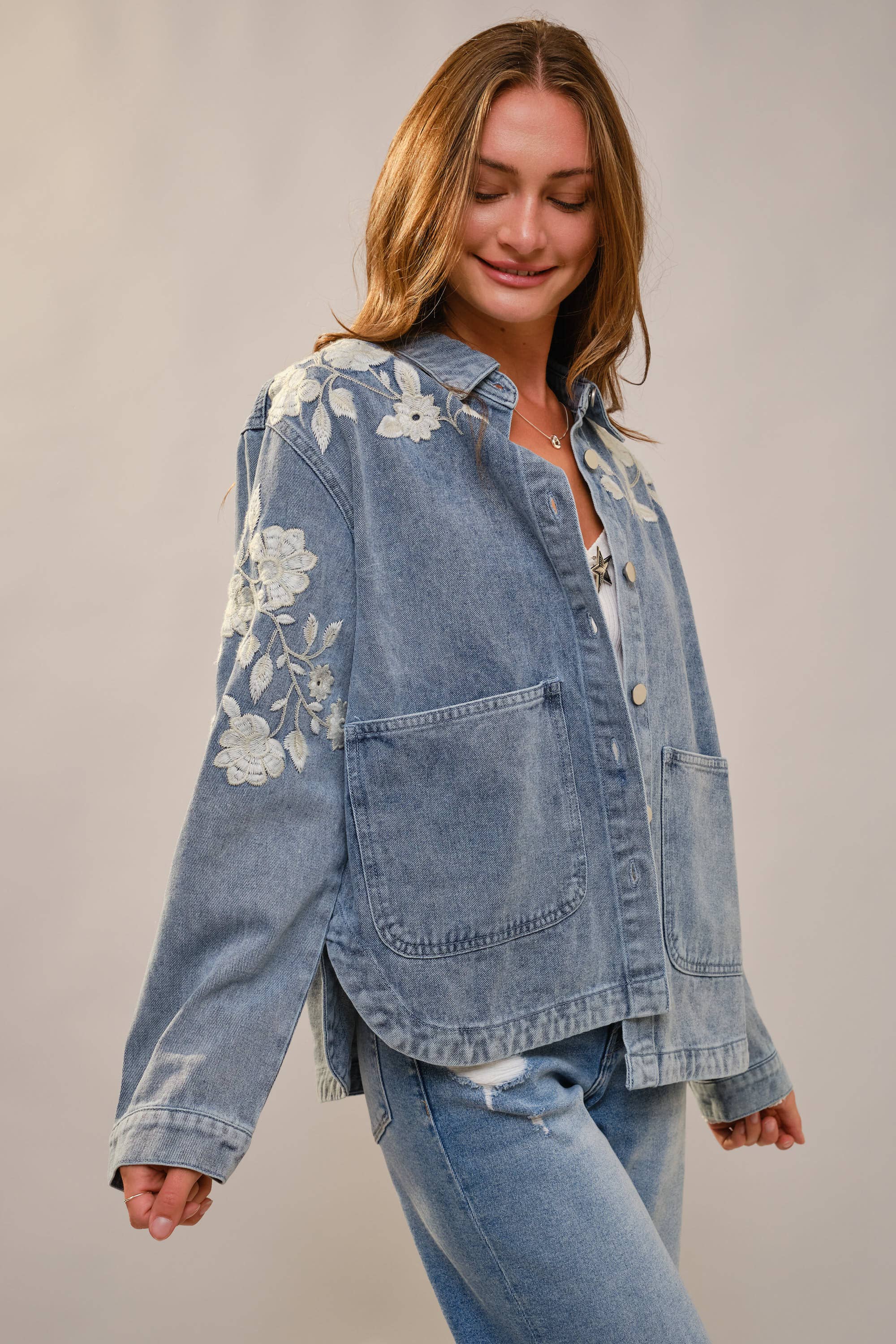 Woman wearing a denim jacket with floral embroidery on a plain background