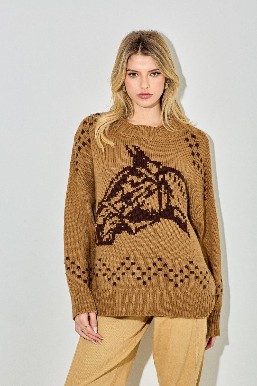 Woman wearing a brown sweater with a horse design on a plain background