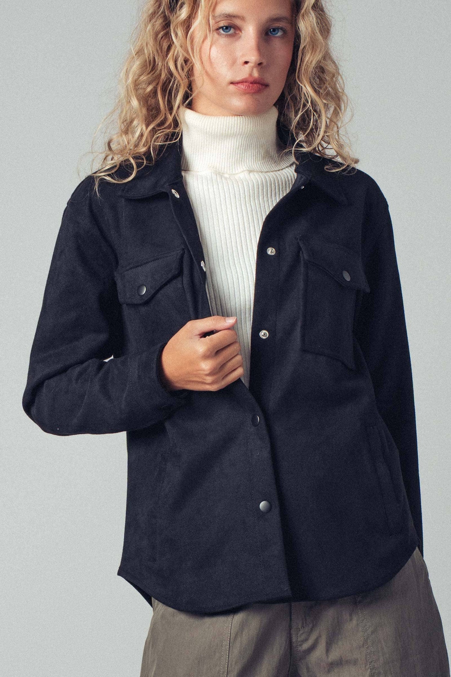 Woman wearing a black jacket over a white sweater on a plain background