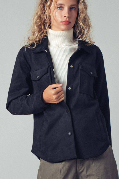 Woman wearing a black jacket over a white sweater on a plain background