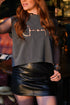 Person wearing a gray crop top with a horse bit design and a black leather skirt.
