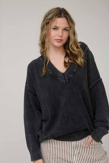 Woman wearing a dark sweater with a V-neckline against a plain background