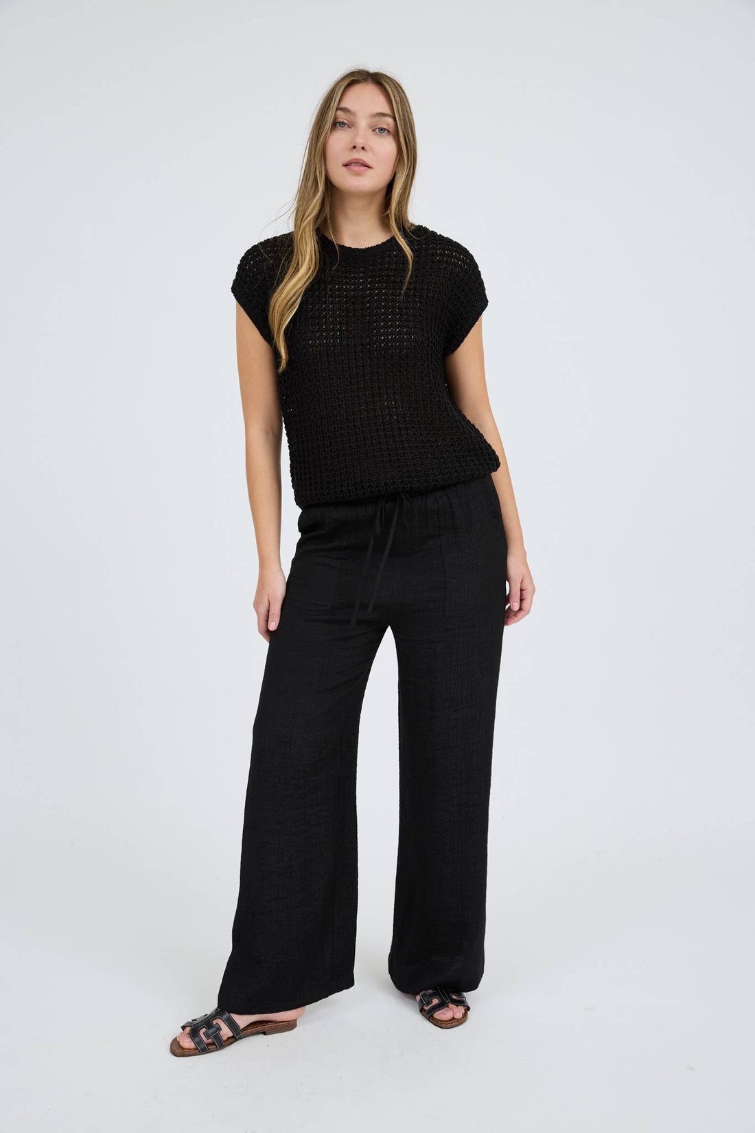 Woman wearing a black patterned top and wide-leg pants on a white background