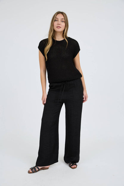 Woman wearing a black patterned top and wide-leg pants on a white background