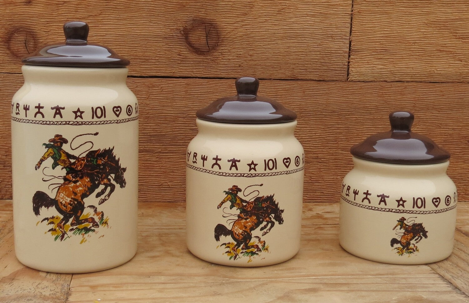Three-piece Western canister set featuring a bronco buster illustration, dark brown rope and brands, and a beige glaze. Sizes include small, medium, and large, all with dark brown lids.
