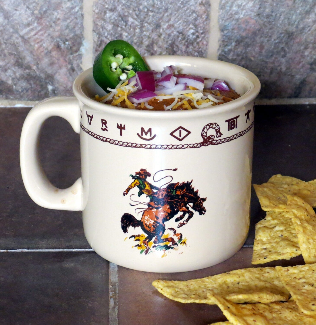 Ivory ceramic western mug featuring a bronco buster illustration with dark brown rope and brand details. Microwave and dishwasher safe, ideal for coffee, chili, cereal, or ice cream.