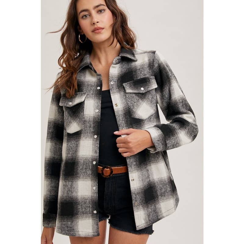 Woman wearing a plaid shirt over a black top and denim shorts on a plain background