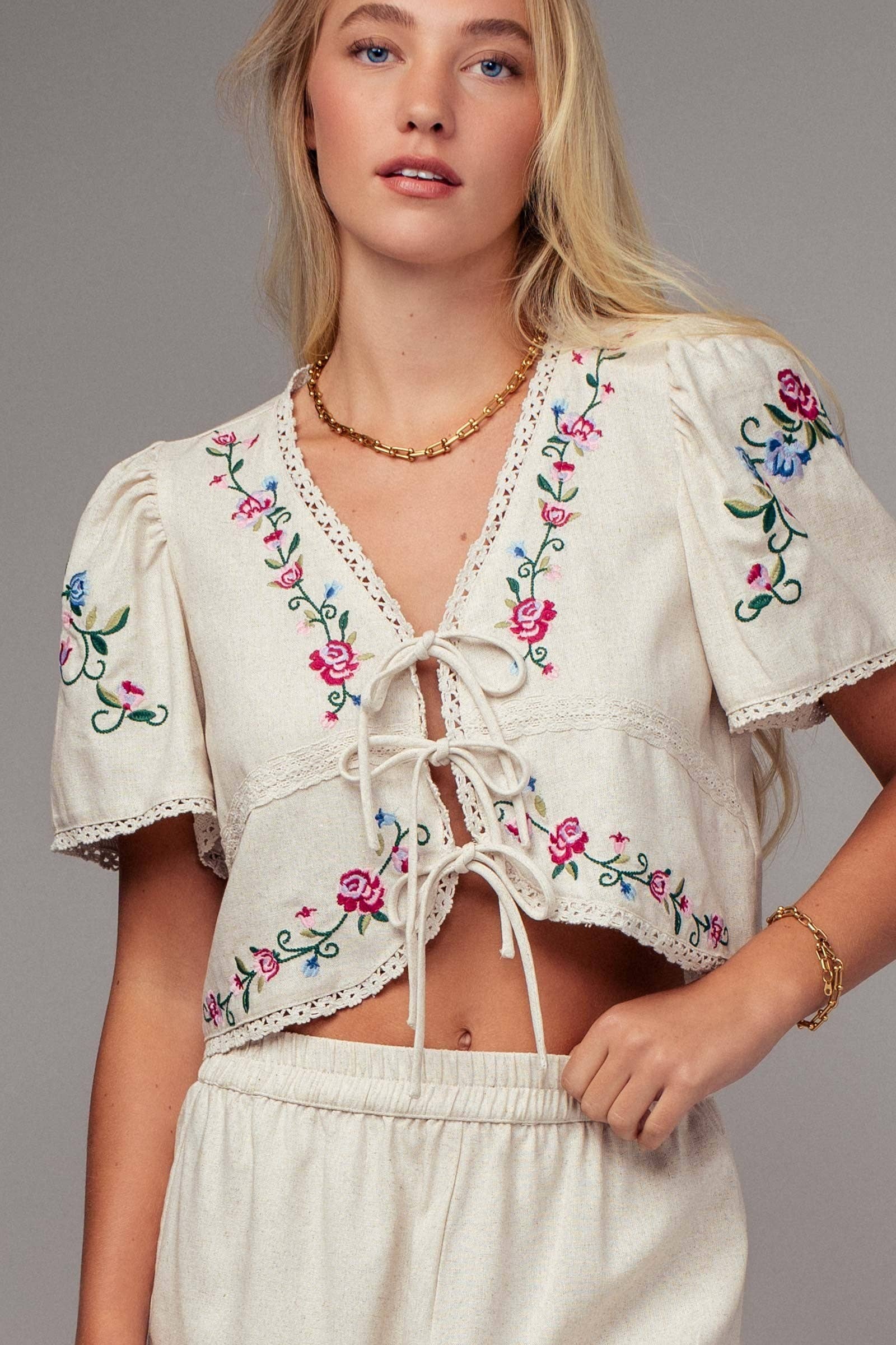 Cream embroidered tie-front crop blouse with floral stitching, lace trim, and short sleeves