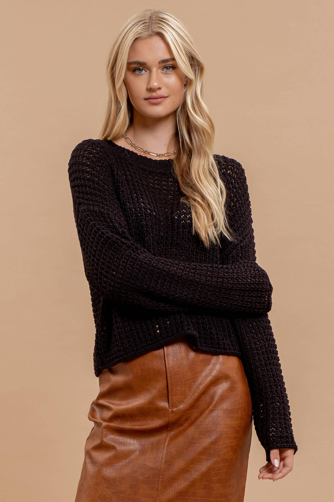 Woman wearing a black knitted sweater and brown leather skirt against a beige background