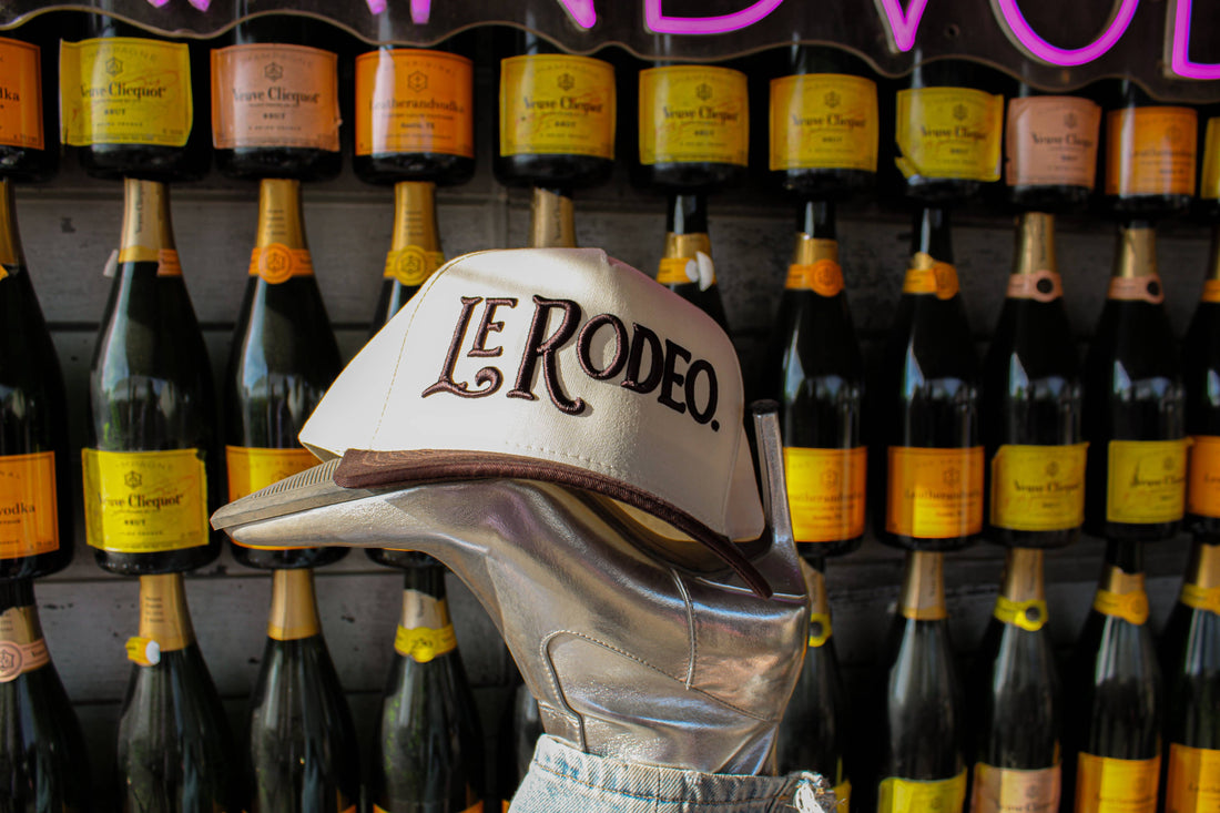 Le Rodeo cap displayed in front of wine bottles with a neon sign in the background