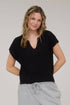 Woman wearing a black top and gray pants against a plain background