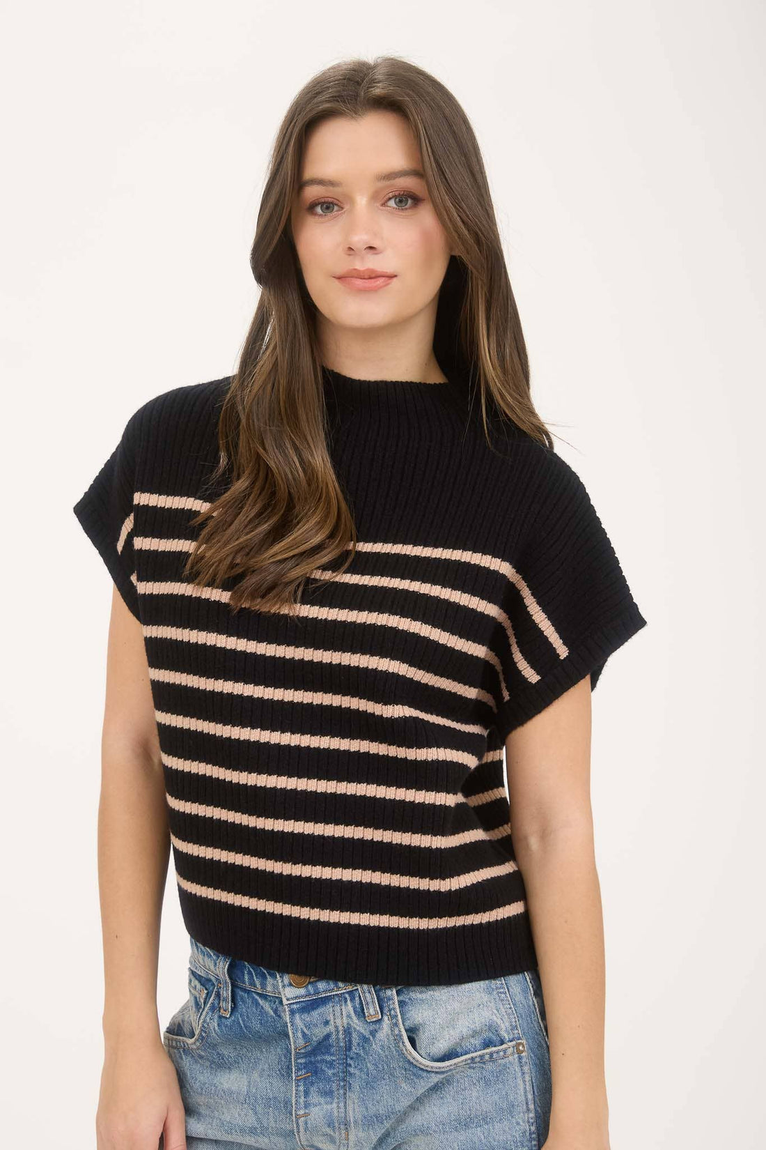 Woman wearing a black and beige striped sweater with blue jeans on a white background