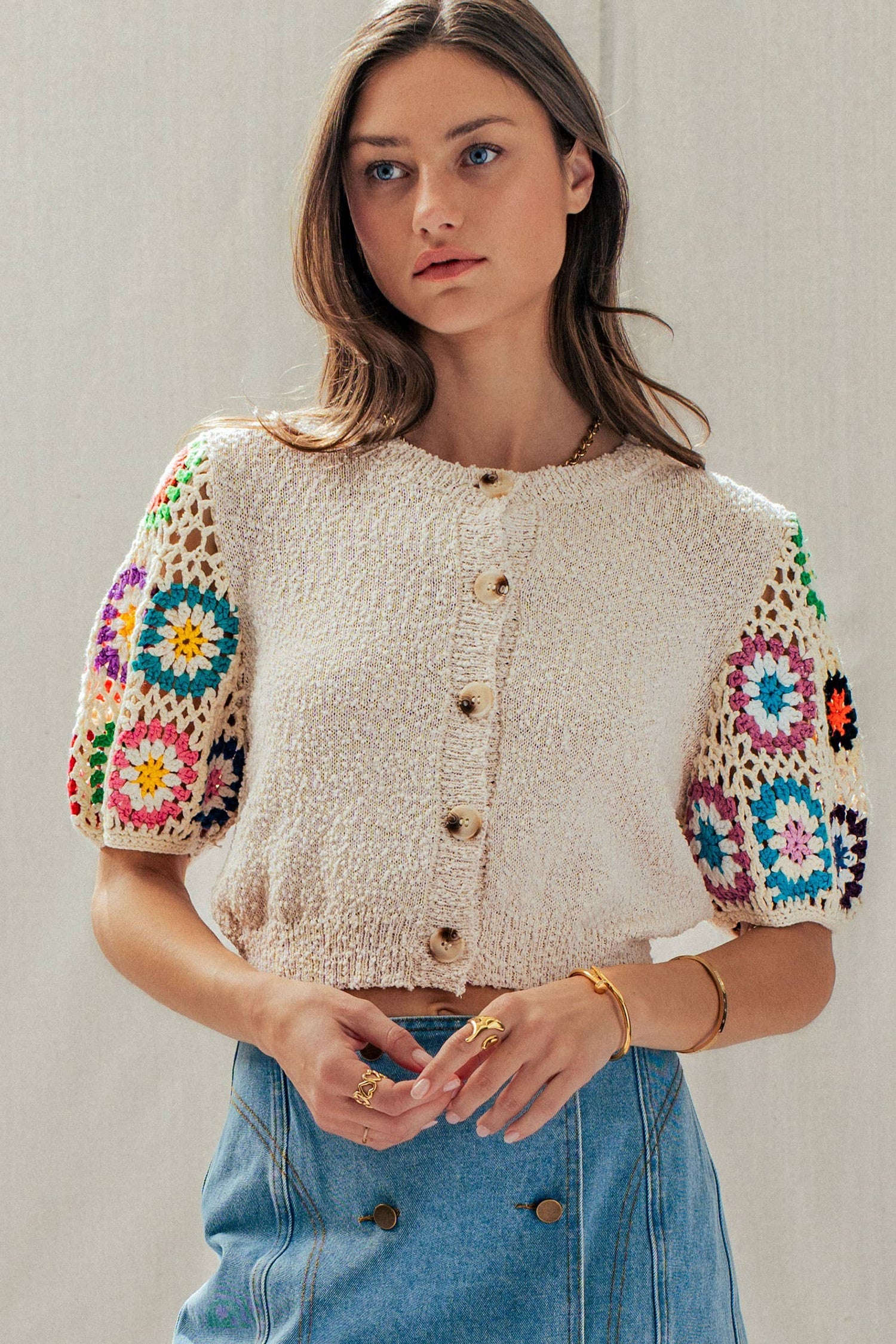 Neutral knit short sleeve cardigan with colorful crochet sleeves, button-front closure, and relaxed cropped fit with western-inspired styling