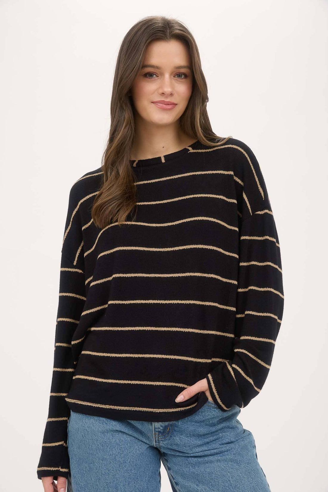 Woman wearing a black and gold striped sweater with blue jeans on a white background