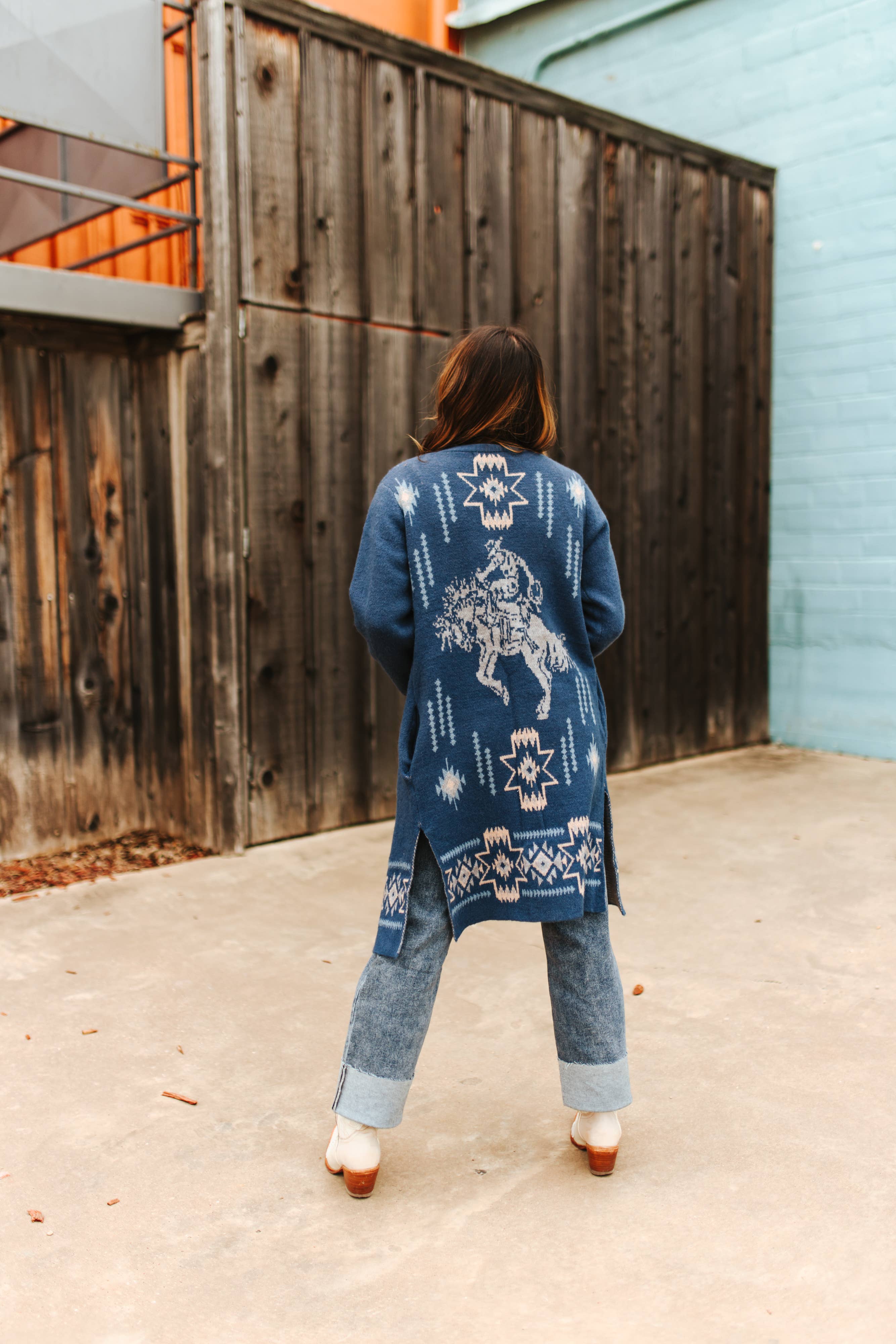 Person wearing a blue patterned cardigan with a wooden fence and light blue wall in the background