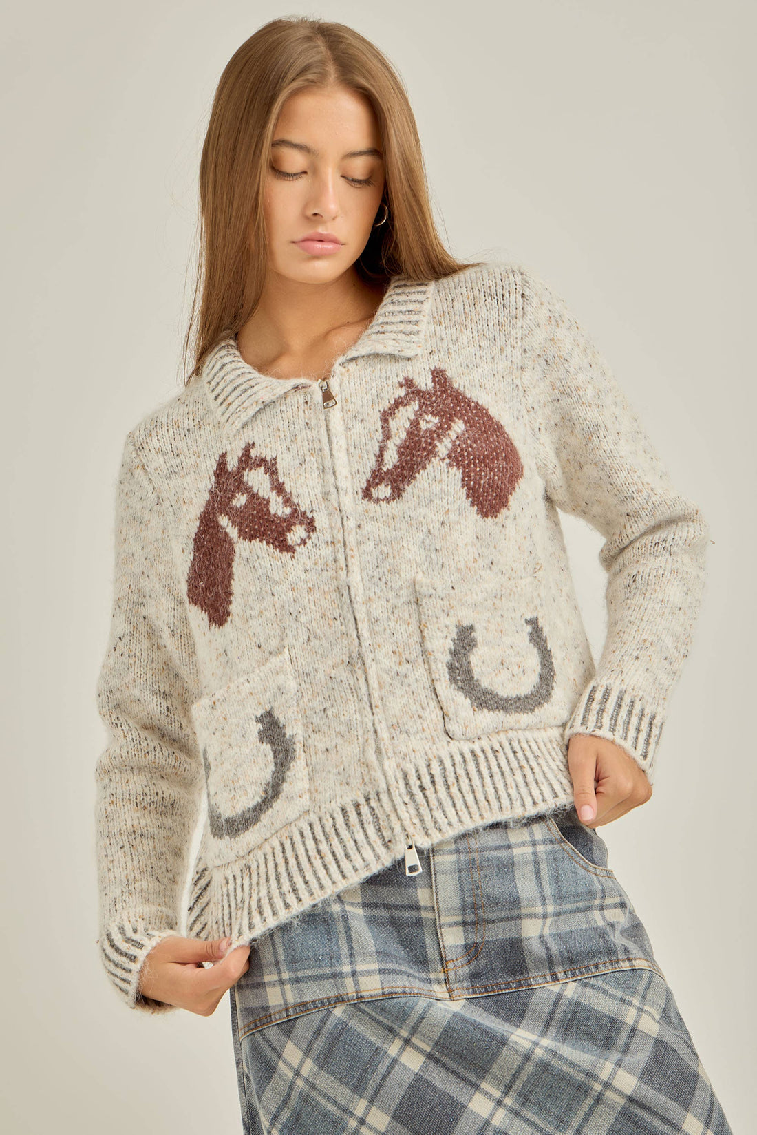 Woman wearing a knitted cardigan with horse and horseshoe patterns on a plain background