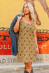 Woman in a patterned dress holding a denim jacket against a colorful mural.