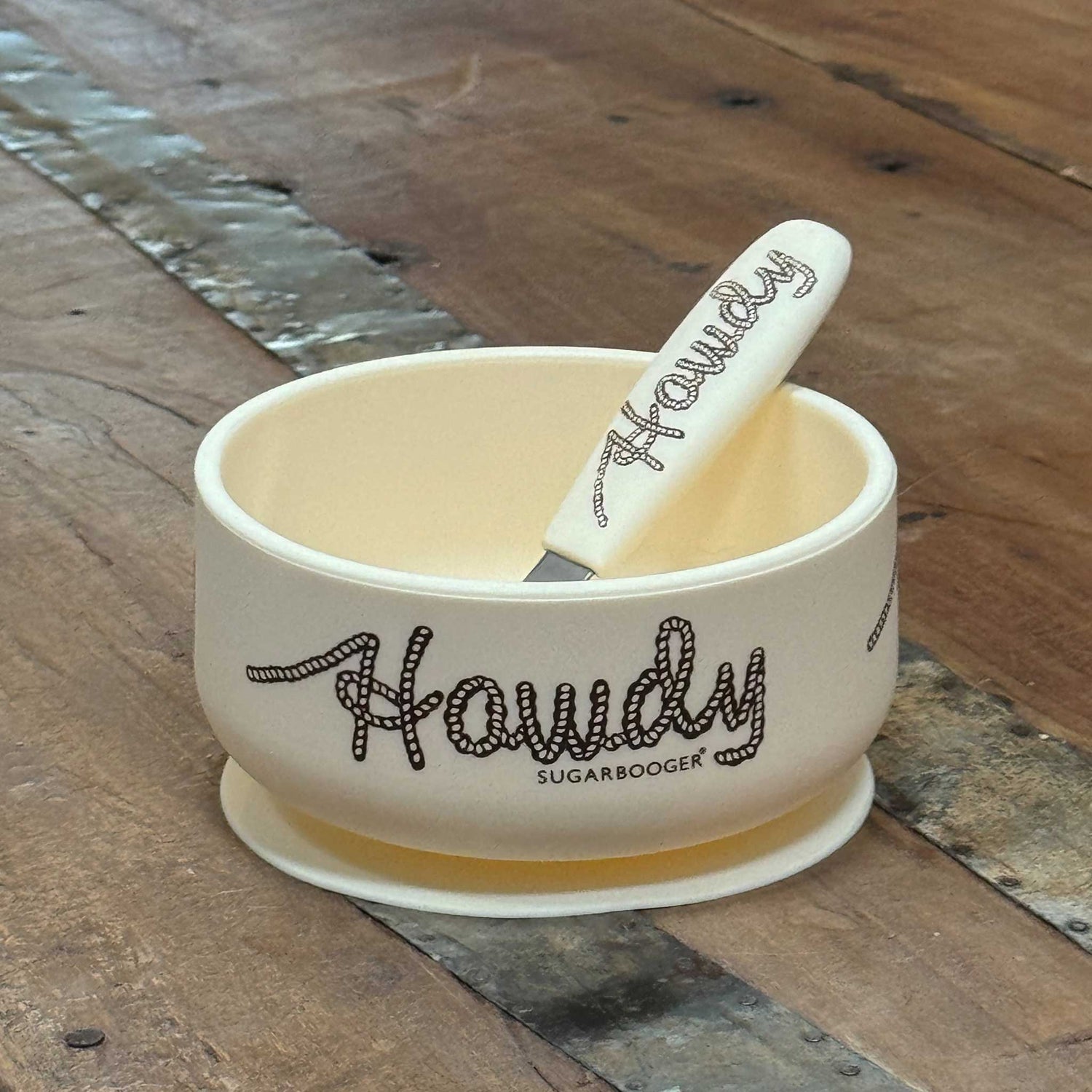 Cream silicone baby suction bowl and spoon set with lasso howdy design, toddler feeding bowl with matching spoon on wood surface