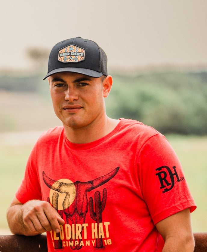 A black trucker hat featuring a colorful Aztec-inspired woven patch with the "Red Dirt Hat Company" logo. Designed for Western and Southwestern style lovers.